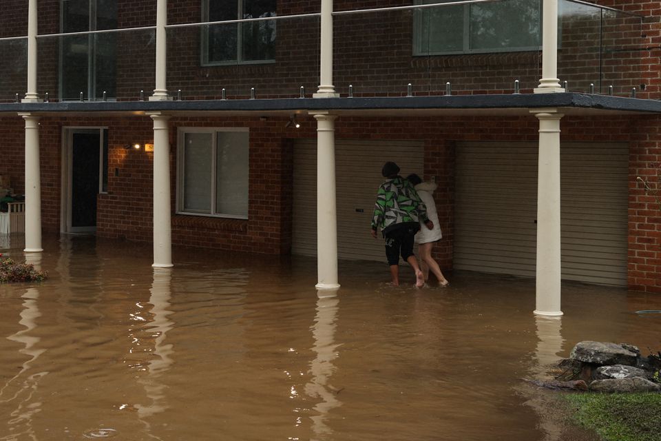 People wade through floodwaters to enter a partially submerged residence following heavy rains in the Windsor suburb of Sydney, Australia, July 5, 2022. Photo: Reuters