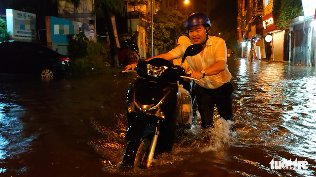 A resident pushes a broken-down motorbike on a flooded street in Hanoi, July 5, 2022. Photo: Nam Tran / Tuoi Tre