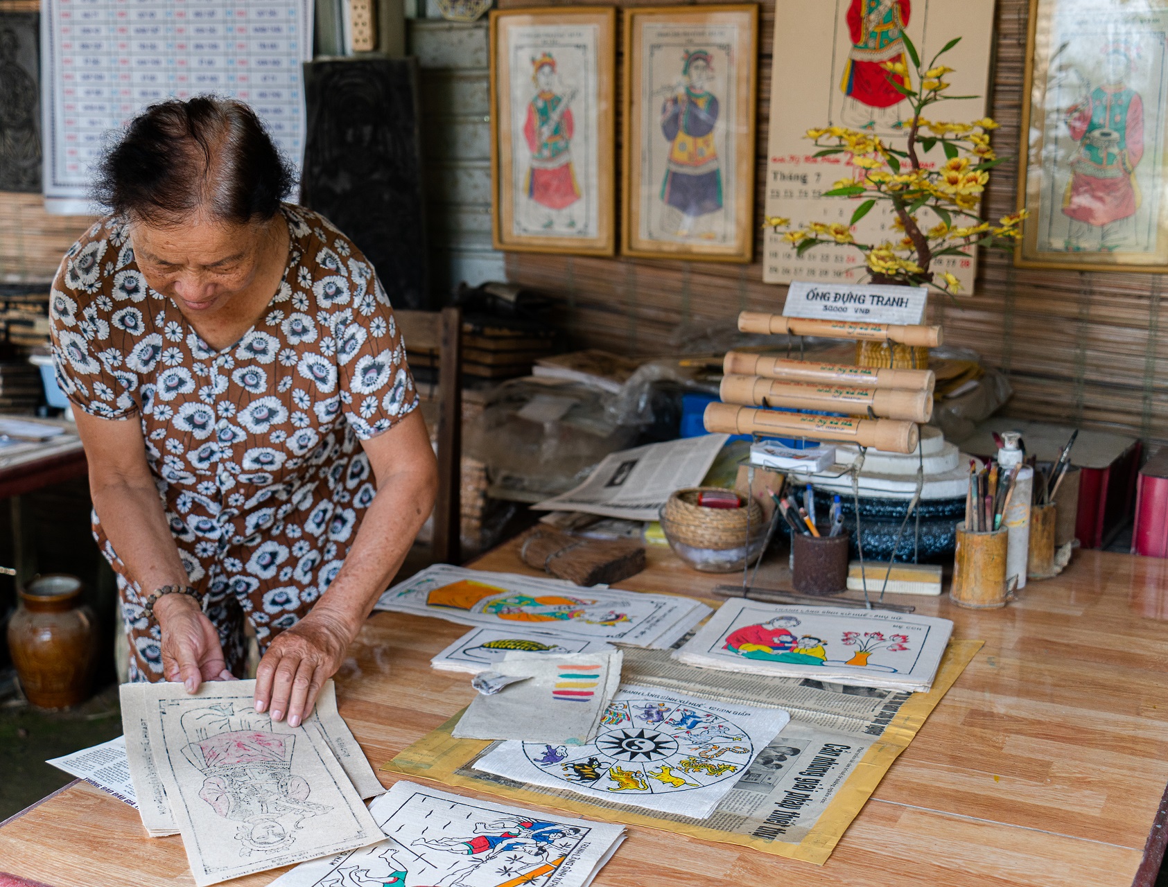 Tran Thi Gai, the wife of artisan Phuoc, introduces paintings of Sinh Village to tourists. Photo: Nguyen Trung Au / Tuoi Tre News