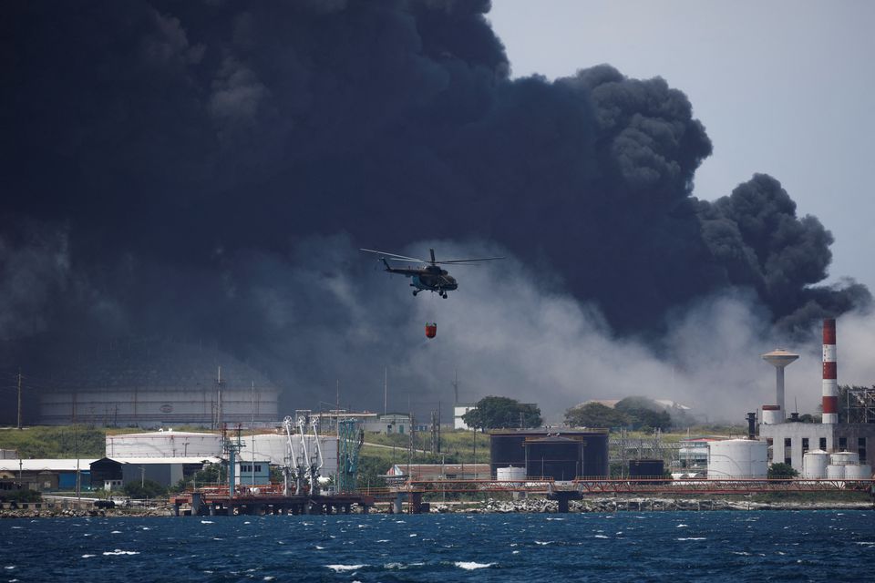 A helicopter prepares to throw water over fuel storage tanks that exploded near Cuba's supertanker port in Matanzas, Cuba, August 6, 2022. Photo: Reuters