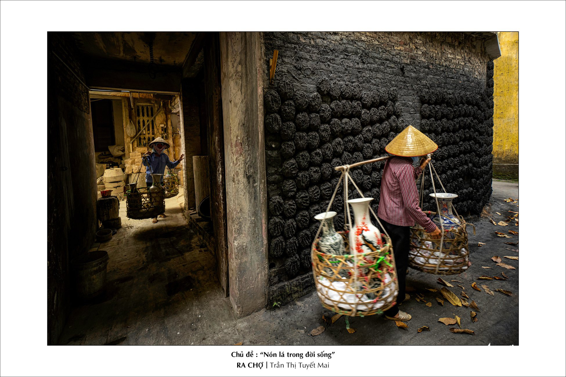Women wearing ‘non la’ hold a bamboo stick over their shoulders while carrying two baskets of vases in this photo on display at the Ho Chi Minh City Photography Association (HOPA) headquarters.