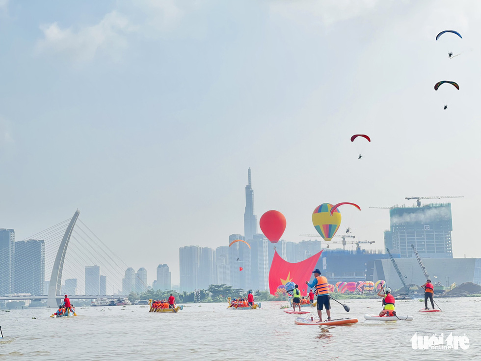 This photo shows standup paddleboarding (SUP) performance on the Saigon River in Ho Chi Minh City, with paragliding flying above them, on September 2, 2022. Photo: Thanh Huy / Tuoi Tre