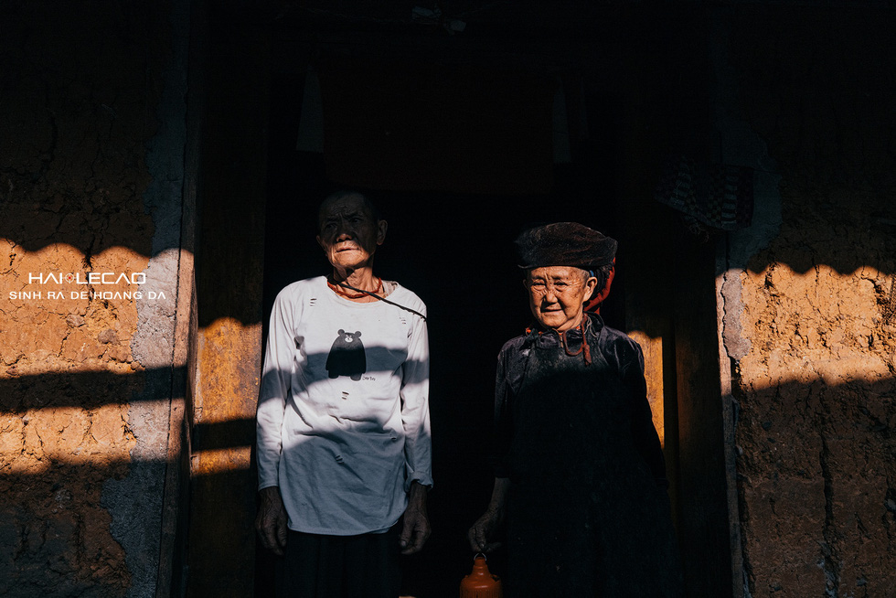 An elderly couple from a local ethnic group stand beneath the eaves of their home as sunlight gleams over them. Photo: Hai Le Cao / Tuoi Tre