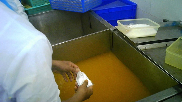 A screenshot shows a person pouring a bag of white powder into a tank in which salt and turmeric are dissolved in water at X.L. Company. Photo: T.Thuong / Tuoi Tre
