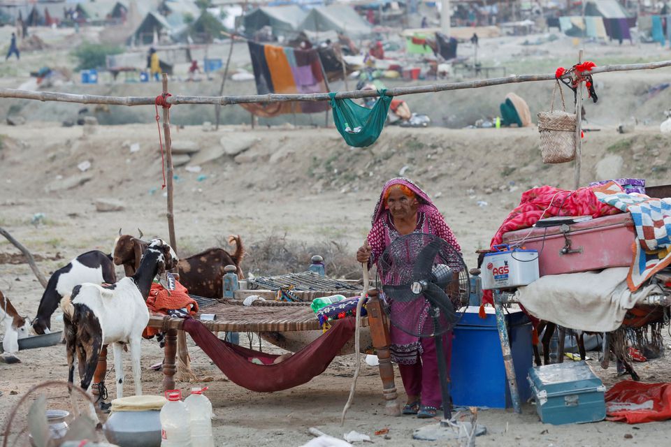 A woman, who became displaced, walks amid her family's belongings while taking refuge in a camp, following rains and floods during the monsoon season in Sehwan, Pakistan September 15, 2022. Photo: Reuters