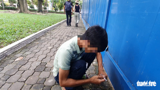 Two tourists walk past a man as he injects narcotics into his bloodstream at 23/9 Park in District 1, Ho Chi Minh City, September 23, 2022. Photo: Minh Hoa / Tuoi Tre