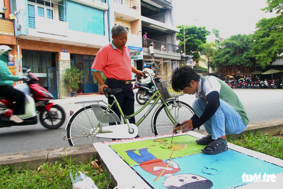 Vu Duy Chinh (holding a bicycle) looks at the drawing Pham Dinh Hai Quan from the Ho Chi Minh City University of Fine Arts is making. Photo: Phuong Quyen / Tuoi Tre