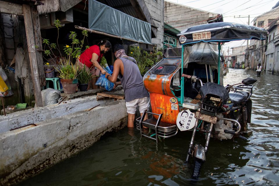 A motorcycle taxi driver helps a passenger with groceries in the flooded coastal town of Hagonoy, Bulacan province, Philippines, September 23, 2022. Photo: Reuters