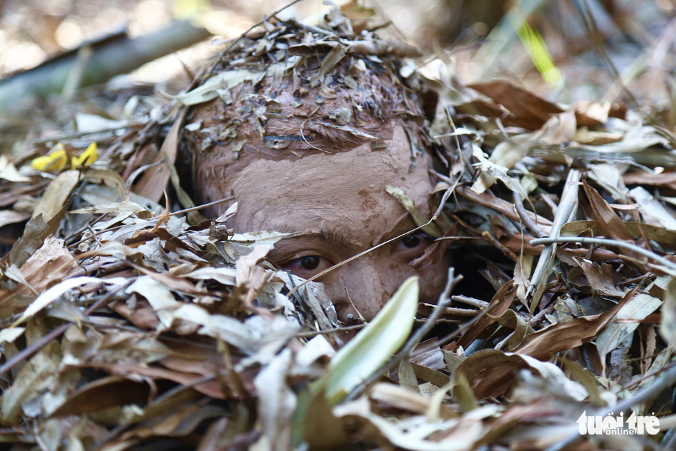 A mobile police officer lies hidden under layers of dry leaves. Photo: Danh Trong / Tuoi Tre