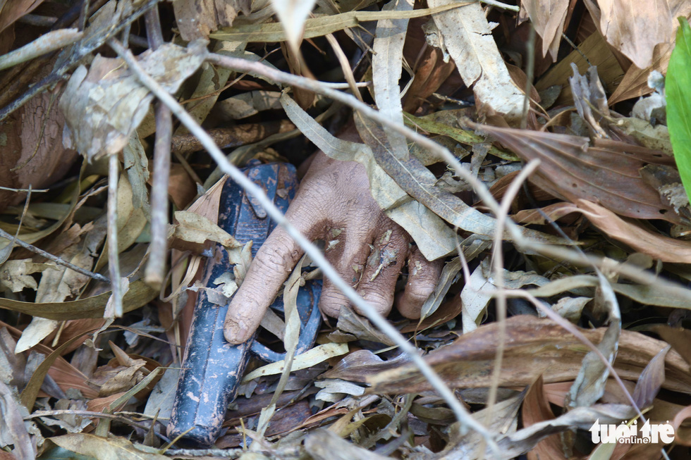 A camouflaged police officer holds a handgun under tree branches and leaves. Photo: Danh Trong / Tuoi Tre