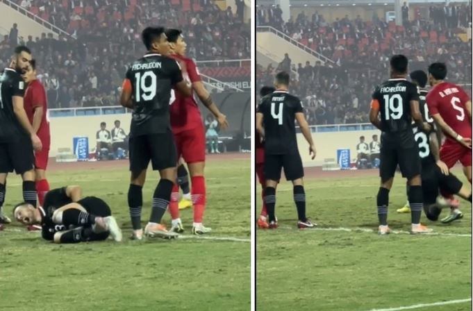 Indonesian midfielder Marc Klok falls on the field while standing next to Vietnamese defender Doan Van Hau (in red, No. 5) who is clasping his hands behind his back during their semifinal second leg at the 2022 AFF Championship in Hanoi on January 9, 2023.