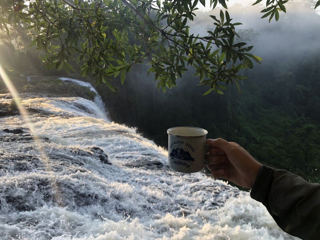 A tourist enjoys a cup of coffee near a waterfall in Mang Den. Photo: Chino tour