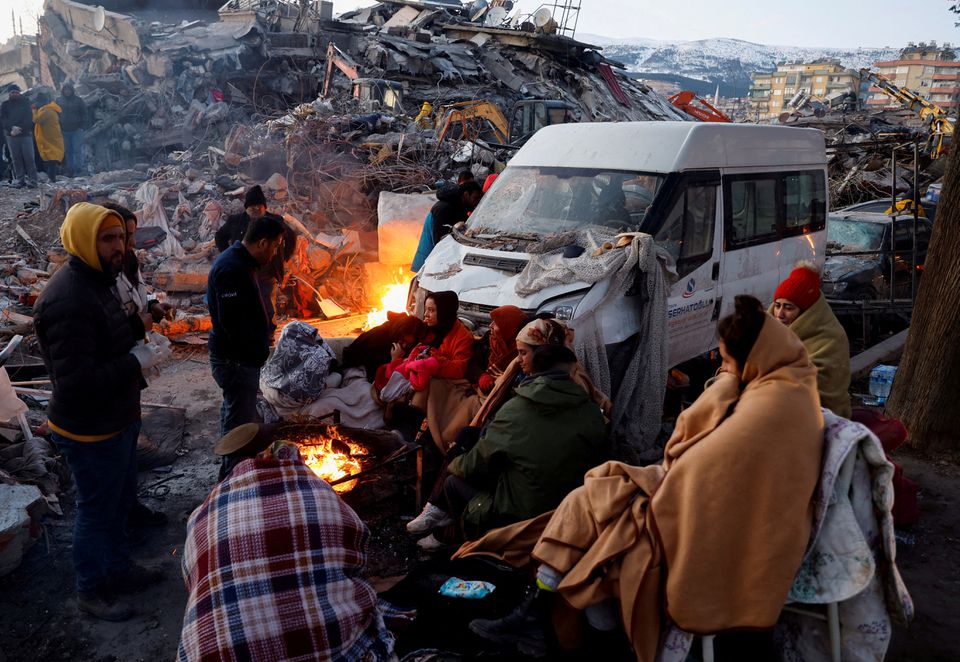 People sit around a fire next to rubble and damages near the site of a collapsed building in the aftermath of an earthquake, in Kahramanmaras, Turkey, February 8, 2023. Photo: Reuters