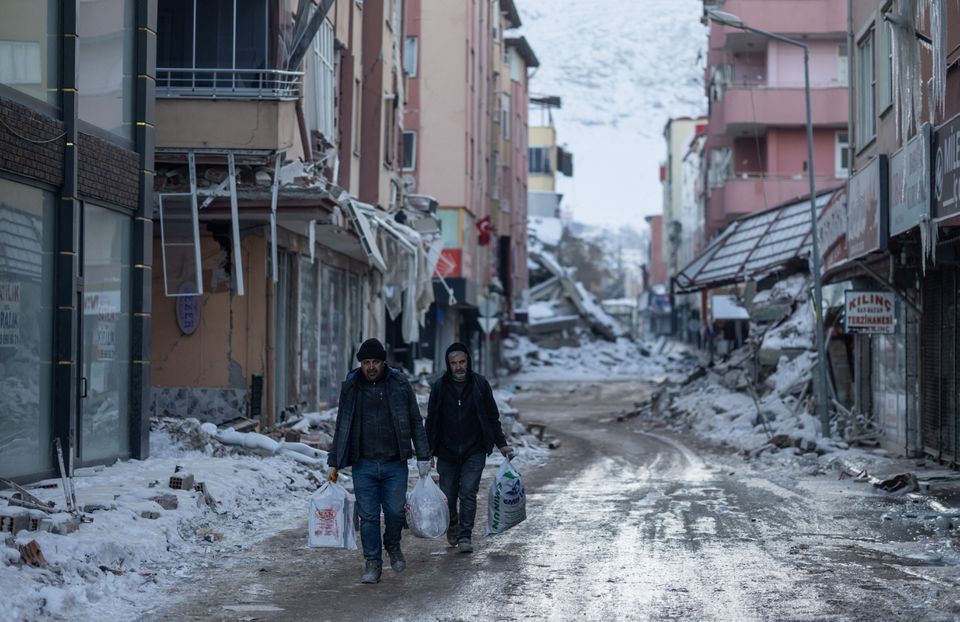 People walk with plastic bags in the street next to destroyed buildings in the aftermath of a deadly earthquake in Elbistan, Turkey February 14, 2023. Photo: Reuters