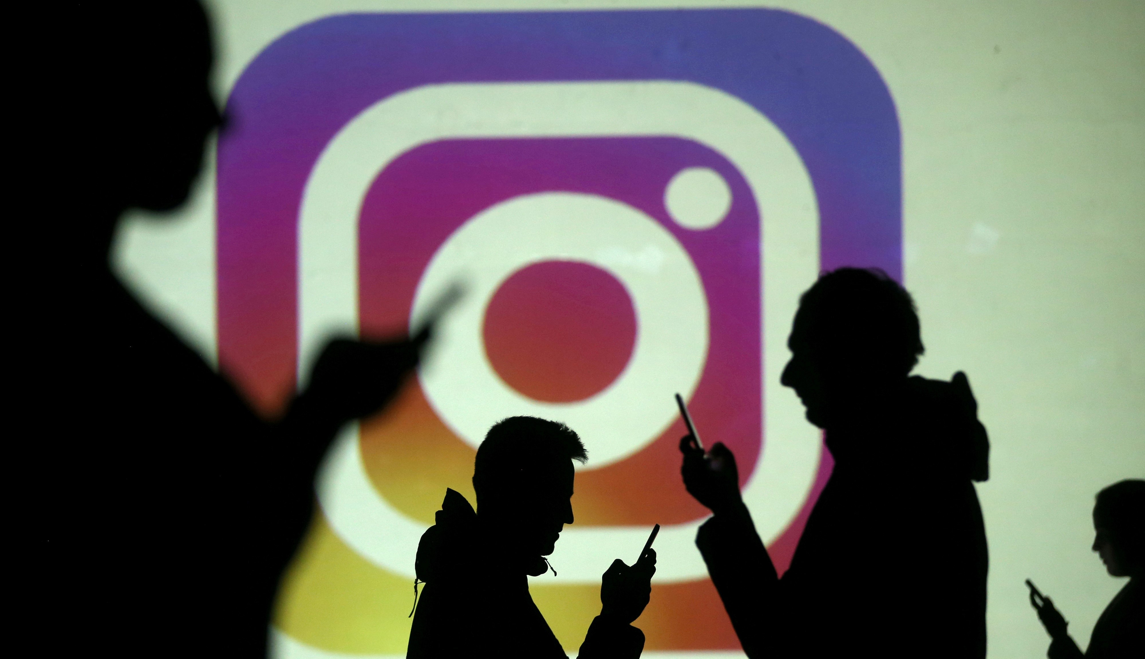 Silhouettes of mobile users are seen next to a screen projection of the Instagram logo in this picture illustration taken March 28, 2018. Photo: Reuters