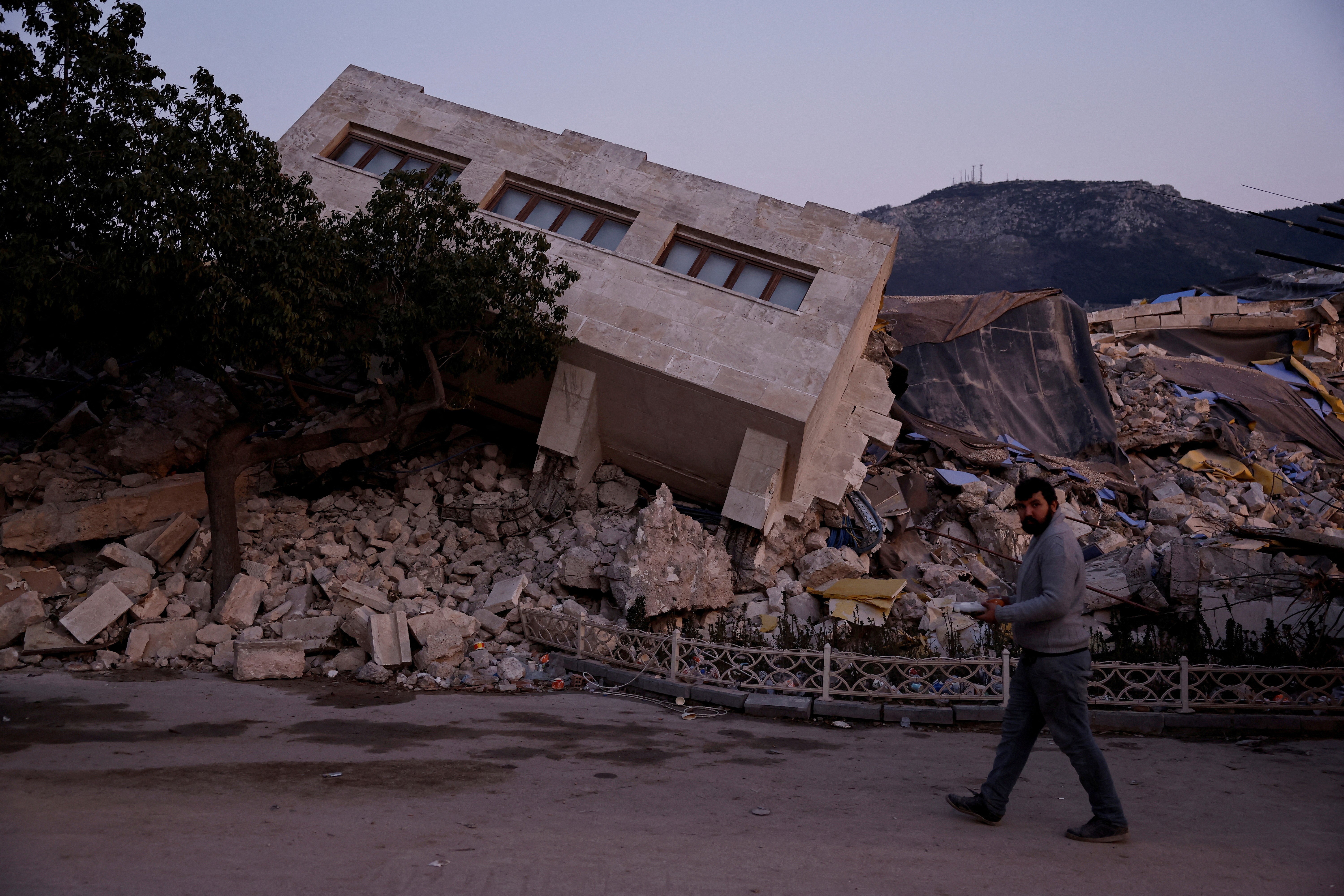 A man walks by a collapsed building and rubble, in the aftermath of a deadly earthquake, in Antakya, Hatay province, Turkey, February 21, 2023. Photo: Reuters