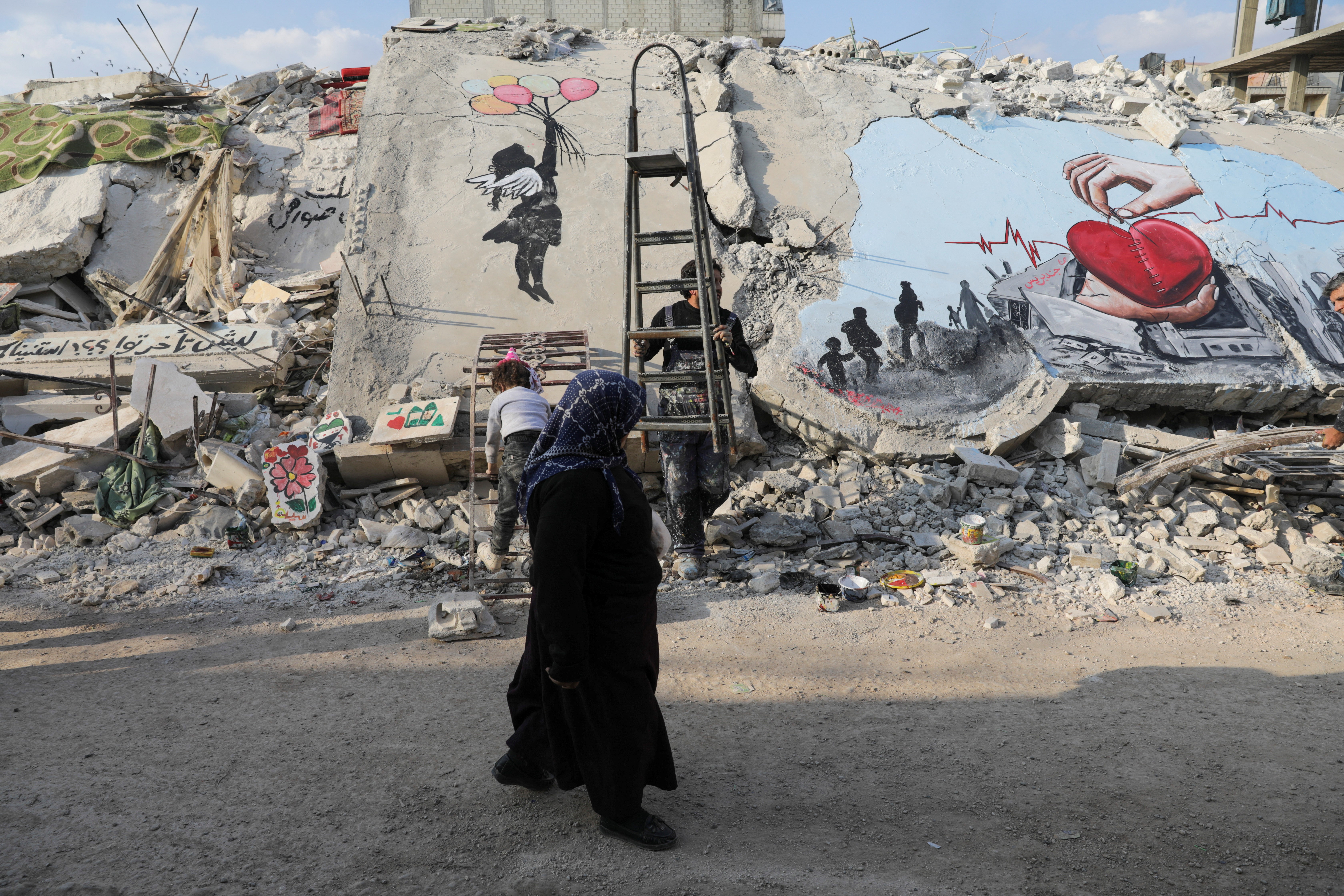 A woman walks past street art on the rubble of damaged buildings in the rebel-held town of Jandaris, in the aftermath of a deadly earthquake, in Syria February 22, 2023. Photo: Reuters