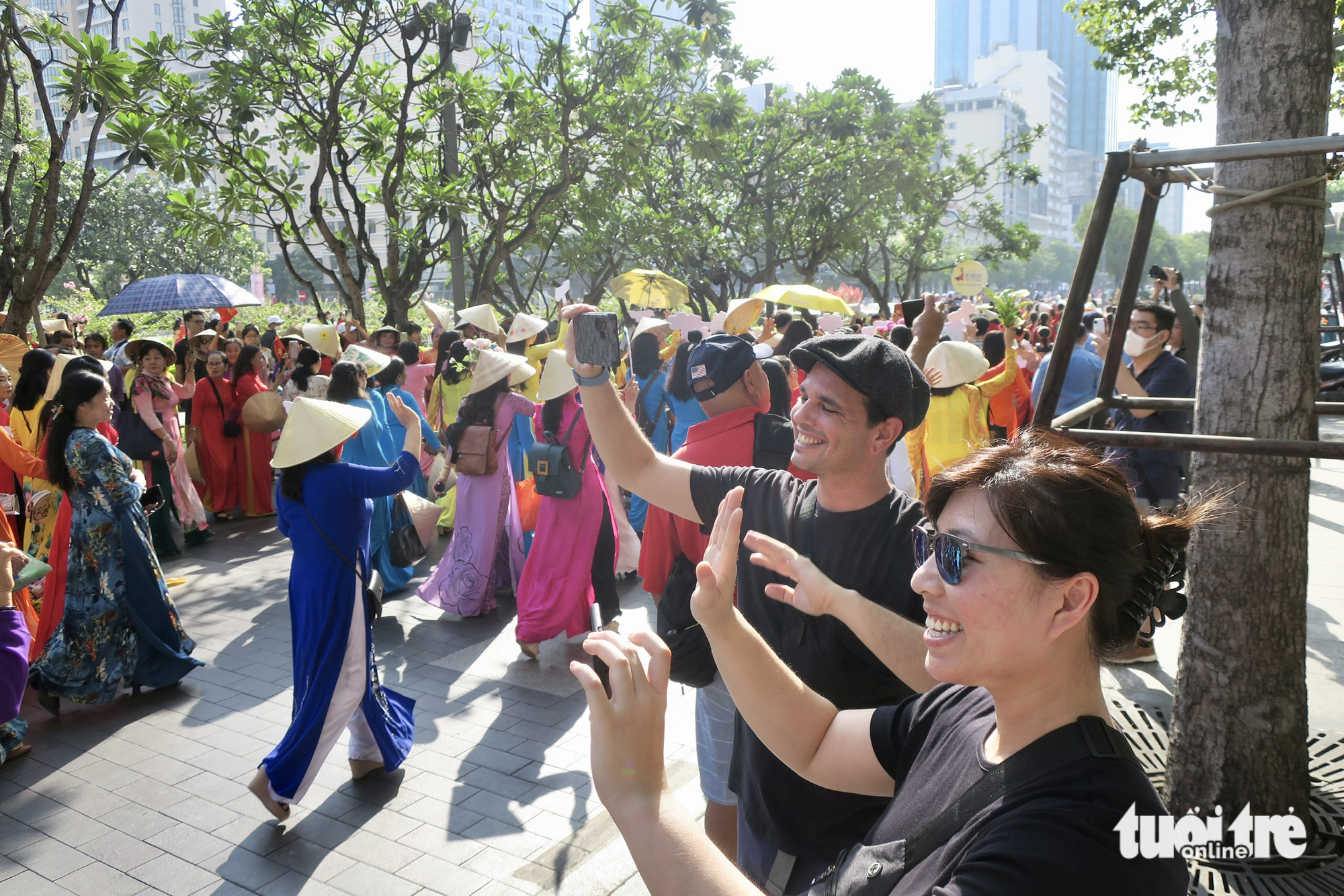 Two U.S. tourists record a video of the ‘ao dai’ parade in Ho Chi Minh City. Photo: T.T.D. / Tuoi Tre