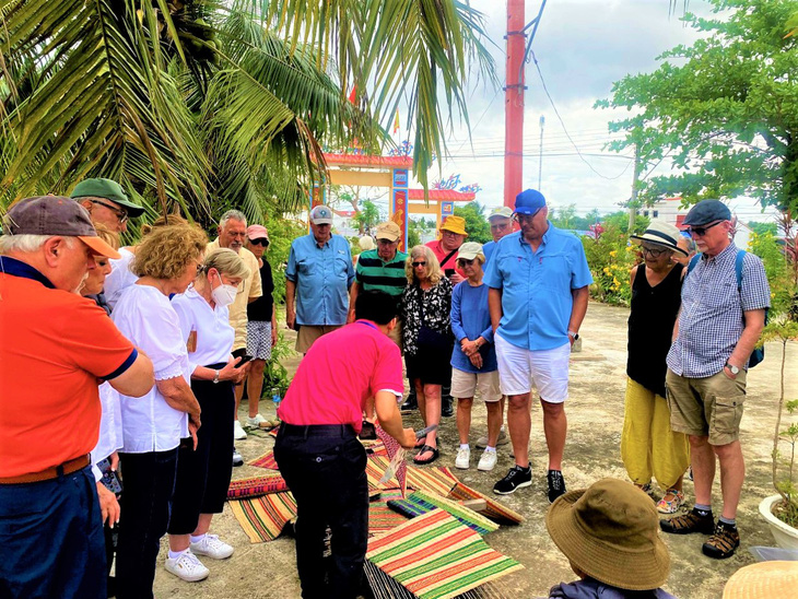 A tour guide shows the tourists how to make sedge mats. Photo: Thuc Nghi / Tuoi Tre
