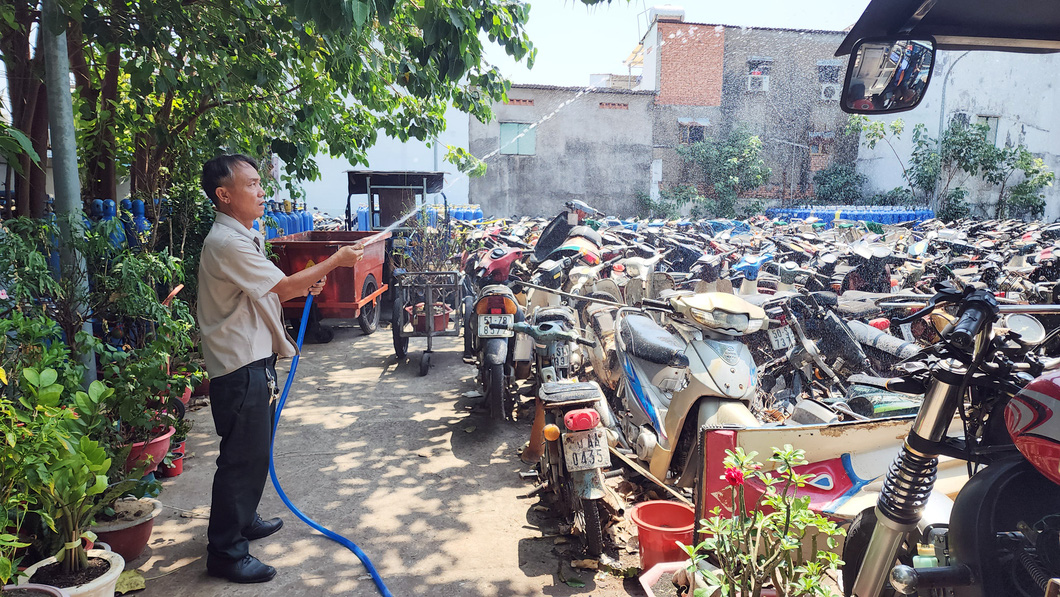An employee at an impoundment area of the traffic order police team under the District 1 Police has to water the impounded vehicles twice a day to cool them off and prevent fires. Photo: Ngoc Khai / Tuoi Tre