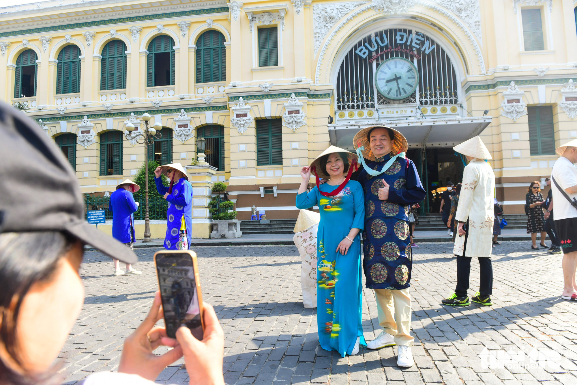 Two Chinese pose for a photo with 'ao dai' (Vietnamese traditional costume) at the Saigon Central Post Office in downtown Ho Chi Minh City on March 17, 2023. Photo: Quang Dinh / Tuoi Tre