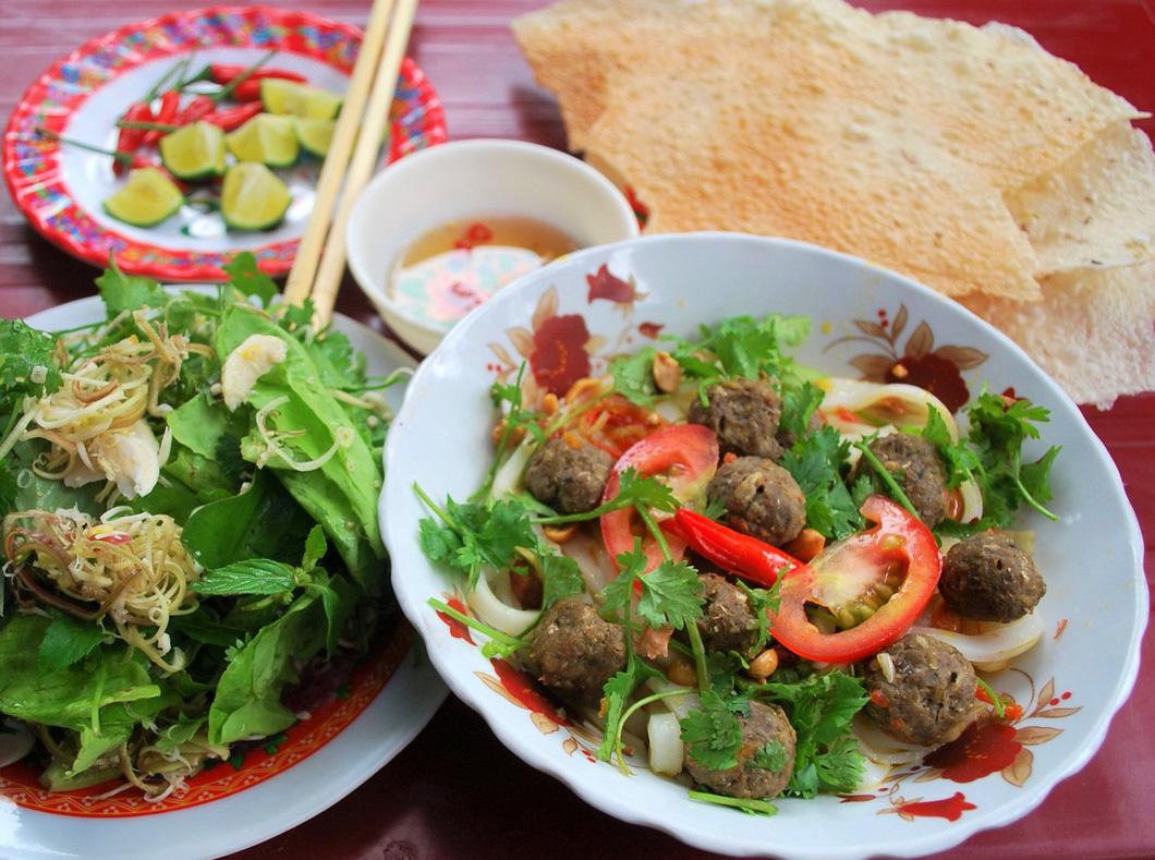 Mi Quang, a noodle dish originated from the central province of Quang Nam, is served with sardine meatballs, fish sauce, and herbs. Photo: Hoa Vang / Tuoi Tre