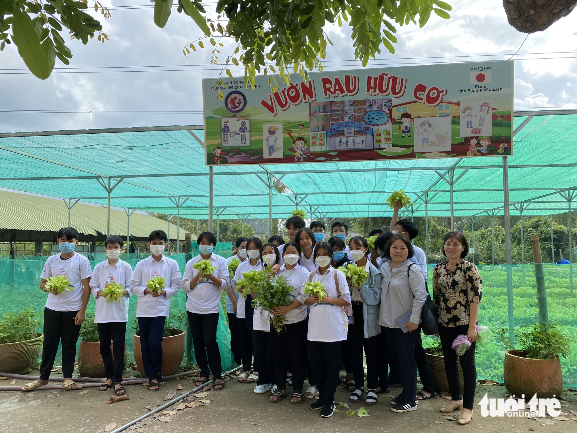 Students and teachers pose for a group photo in front of a school vegetable garden