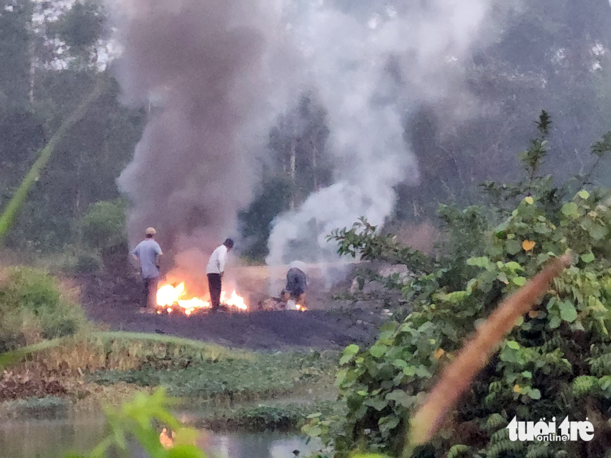Three men burn garbage at Hai Phung Bridge at dawn on March 21, 2023. Photo: Tuoi Tre