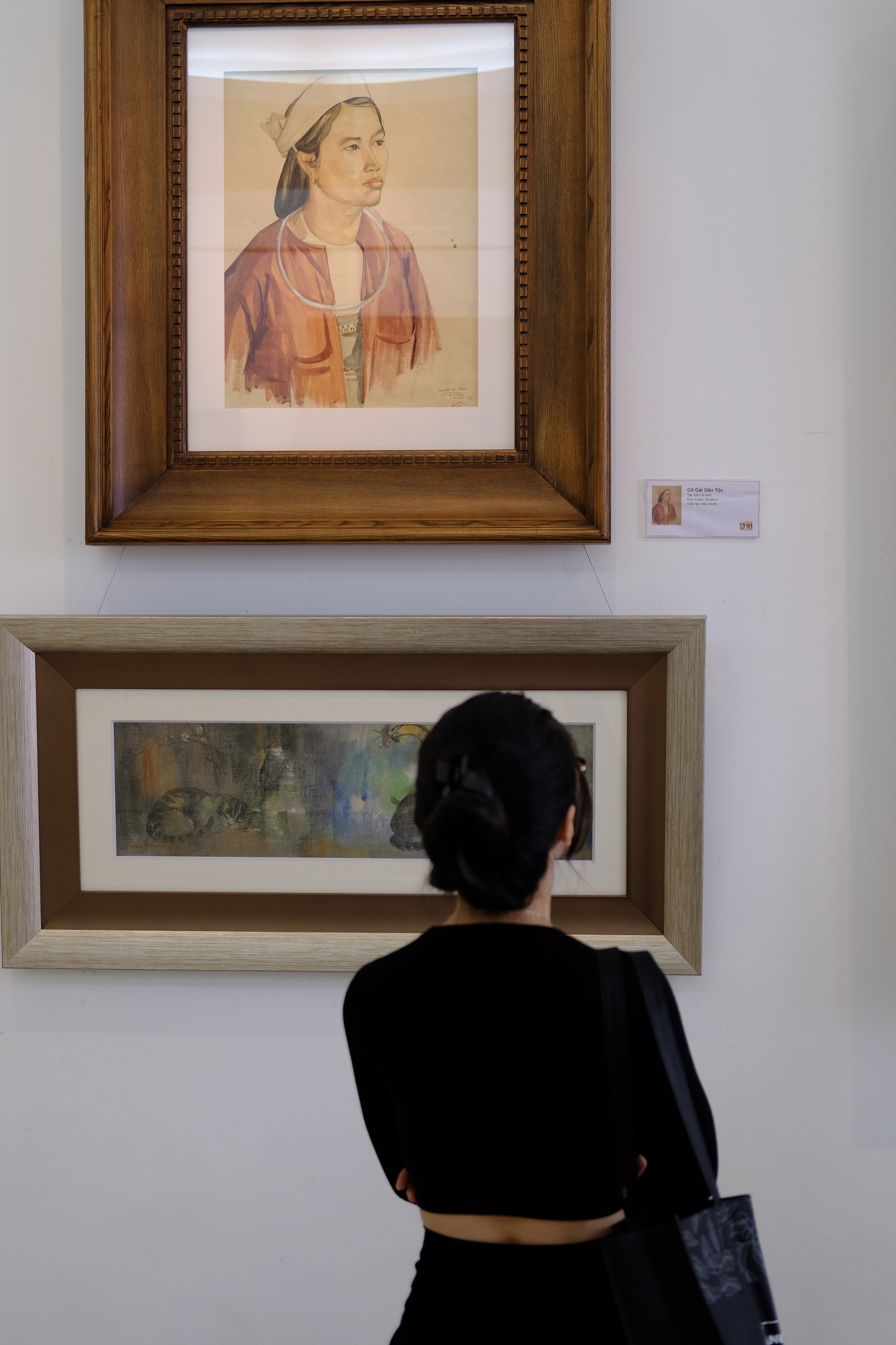 A visitor looks at the watercolor painting titled “Co Gai Dan Toc” (above) by Le Vinh and a silk painting titled “Meo” by Dang Quy Khoa. Photo: Phuong Tran / Tuoi Tre News