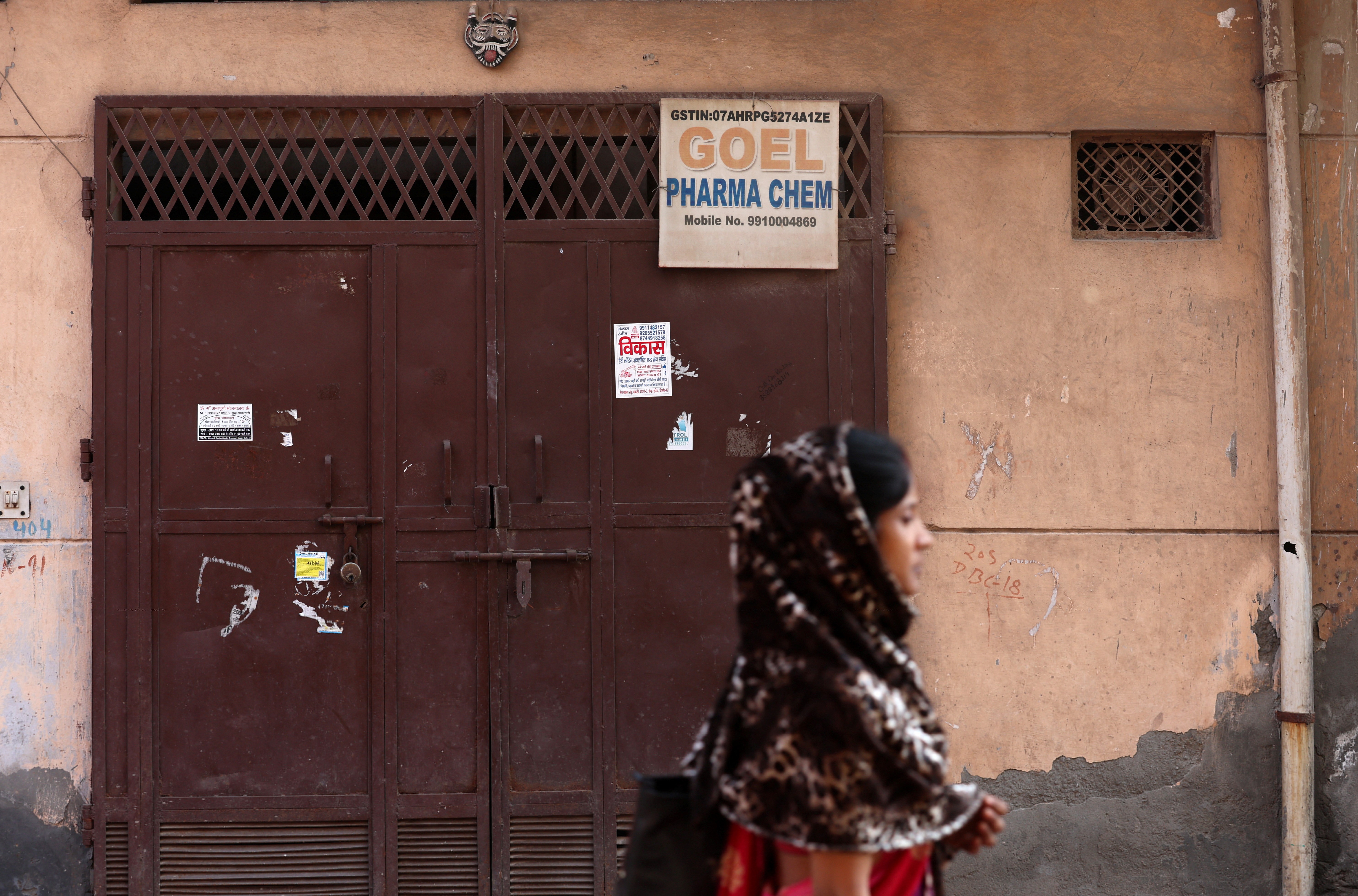 A woman walks past the closed gate of Goel Pharma Chem, a chemicals trading firm that according to government officials supplied raw ingredients to Maiden Pharmaceuticals whose cough syrups were linked to the deaths of dozens of children in Gambia, in New Delhi, India, April 3, 2023. Photo: Reuters