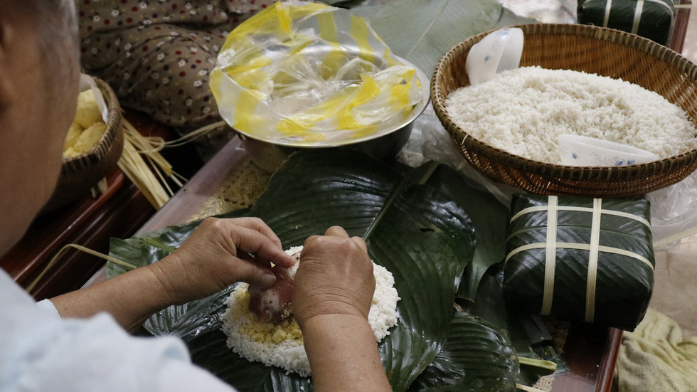 A woman puts pork and ground mung beans onto rice to make banh chung. Photo: Tuoi Tre