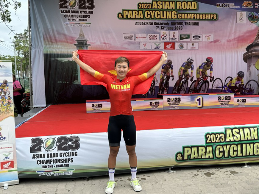 Vietnamese cyclist Nguyen Thi That proudly holds the Vietnamese national flag after her stunning victory at the 2023 Asian Road and Para Cycling Championships in Thailand on June 12, 2023. The photo captures the remarkable moment of her triumph. M.C.H.