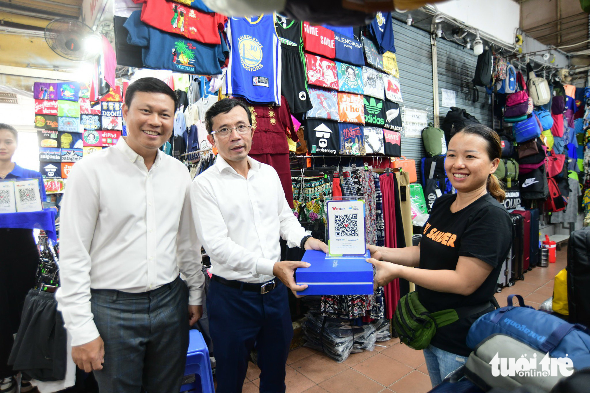 Ngo Thi Ai Van (R), owner of a baggage stall at Ben Thanh Market, receives a VietQR code from Tran Xuan Toan (C), deputy editor-in-chief at Tuoi Tre (Youth) newspaper. Photo: Tuoi Tre