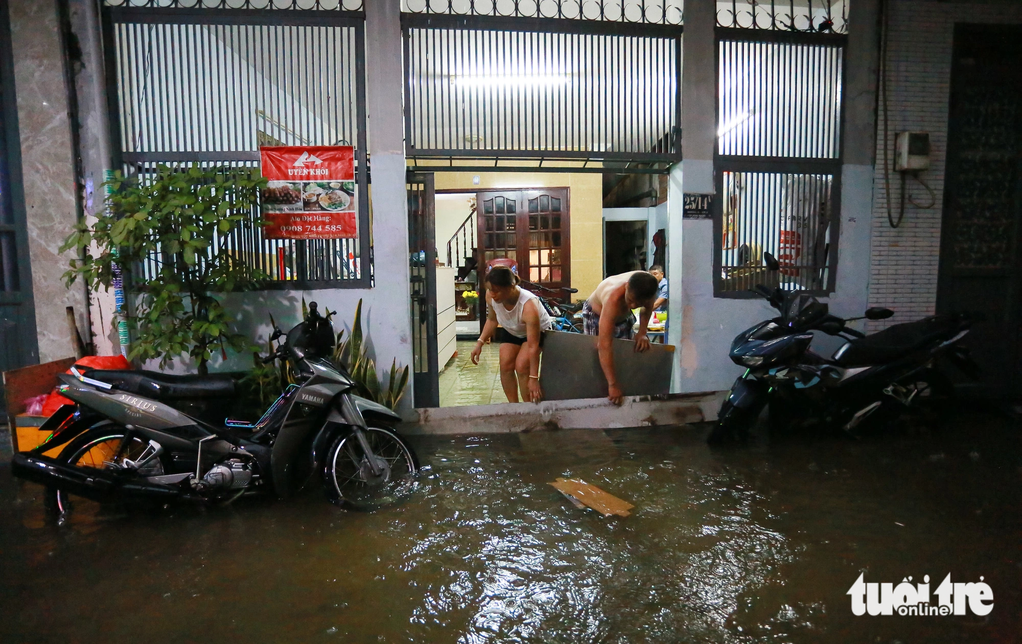 Two local residents use pieces of wood and other materials to prevent rainwater from flowing into their homes along Street No.6 in Hiep Binh Phuoc Ward, Thu Duc City, under the jurisdiction of Ho Chi Minh City on July 5, 2023. Photo: Chau Tuan / Tuoi Tre