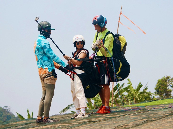 A professional equips safety gadgets for a tourist before taking off for paragliding in Hon En Mountain, Nha Trang City, Khanh Hoa Province. Photo: Do Phuong / Tuoi Tre