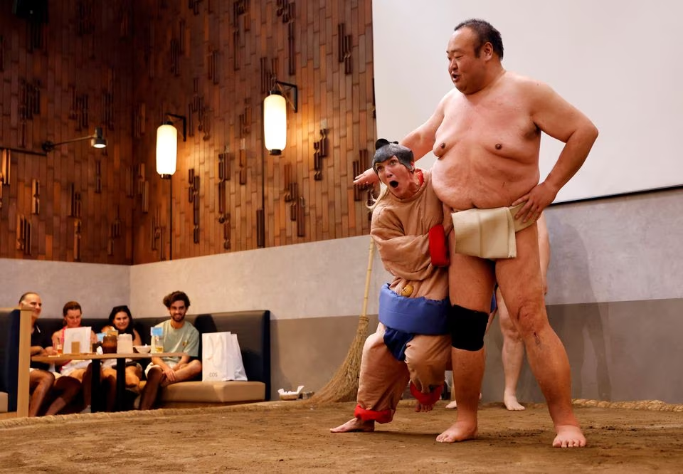 Nadine, a 43-year-old tourist from the U.S., wearing a sumo wrestler costume, tries to spar against former sumo wrestler Towanoyama on the sumo ring at Yokozuna Tonkatsu Dosukoi Tanaka in Tokyo, Japan June 30, 2023. Photo: Reuters