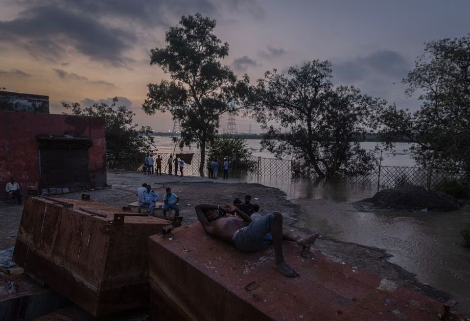 A man rests as others stand on the banks of overflowing river Yamuna in New Delhi, India, July 12, 2023. Photo: Reuters