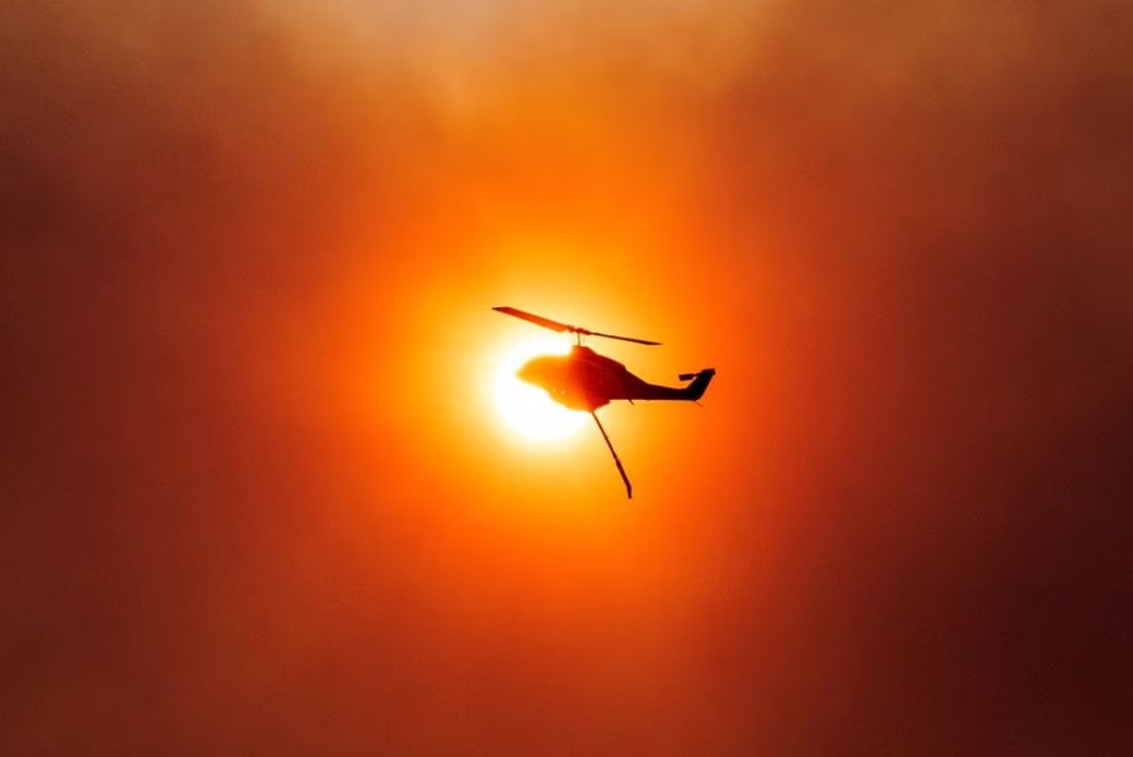 A firefighting helicopter is silhouetted in front of the sun as a wildfire burns in Mandra, Greece, July 18, 2023. Photo: Reuters