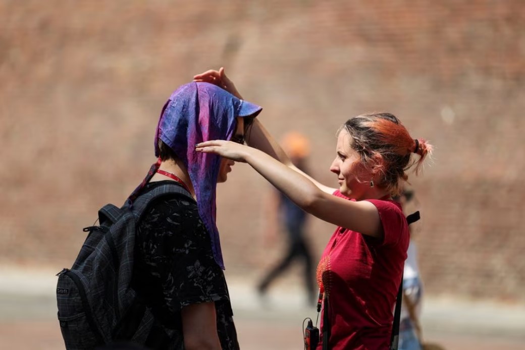 A woman places a wet head scarf to protect a man from the sun in Bologna, Italy, July 18, 2023. Photo: Reuters