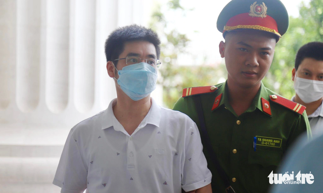 Police officers take Hoang Van Hung (in white T-shirt), an ex-investigator from the Ministry of Public Security’s Security Investigation Authority, to the court in Hanoi. Photo: Danh Trong / Tuoi Tre