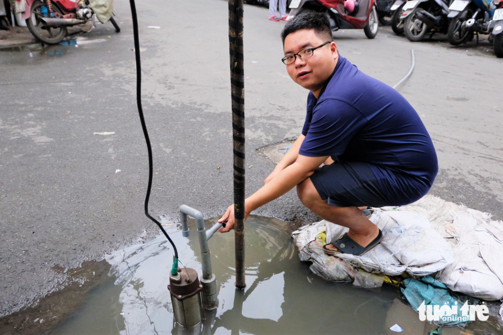 Huynh Huu Hieu, a resident at An Quang apartment building, sits next to his pump which works at its full capacity but fails to pump all of the stagnant water in front of his apartment. Photo: Phuong Nhi / Tuoi Tre